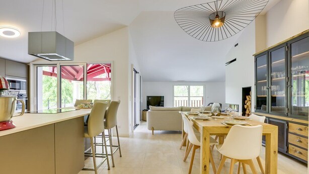 A modern kitchen with a dining area, large windows, and a view of the outdoors.