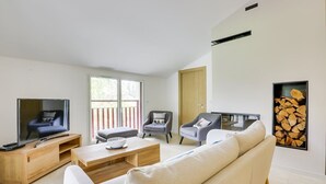 A modern living room with a flat-screen TV, two sofas, a coffee table, and a fireplace with a wood display.
