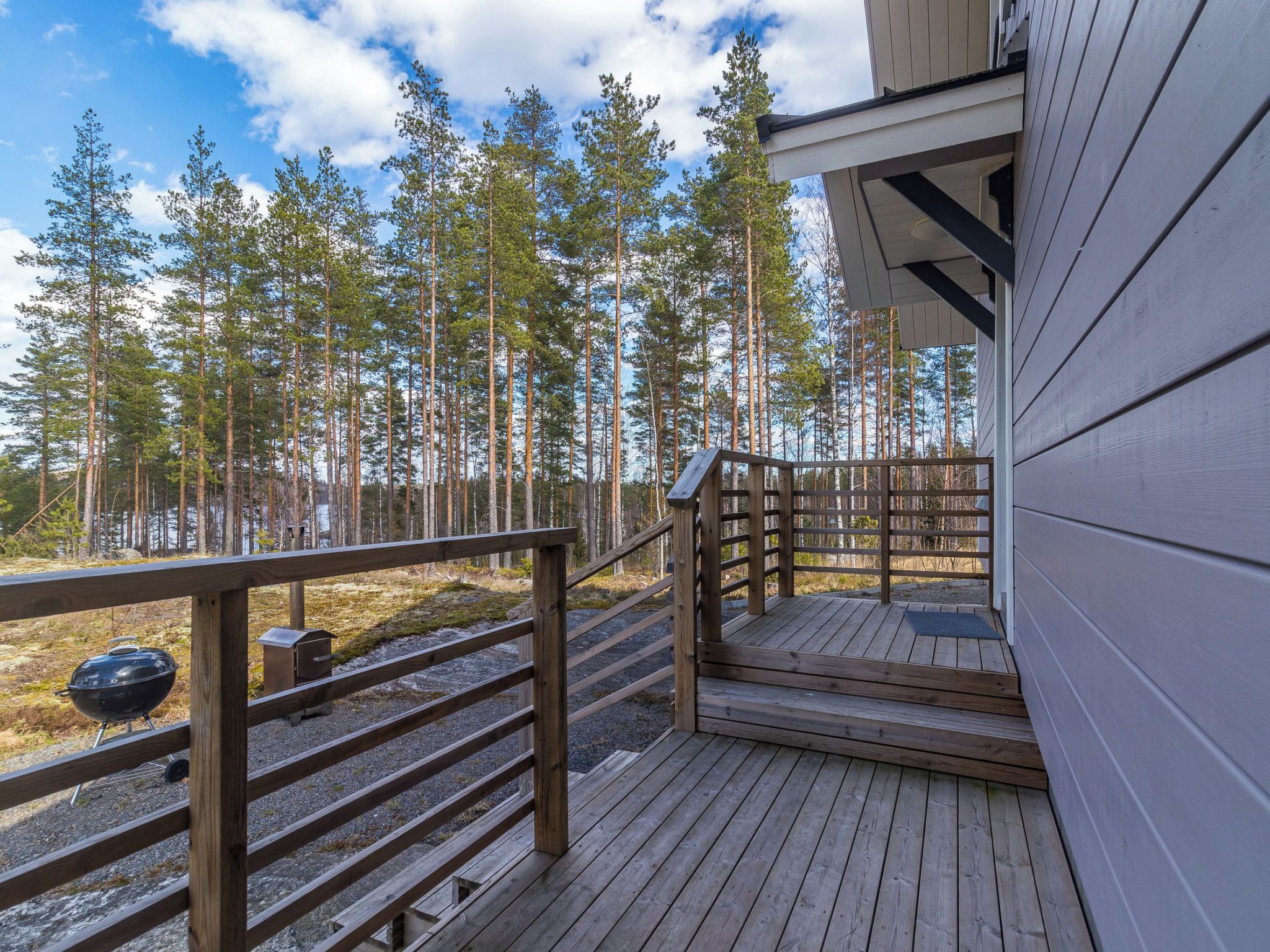 A wooden deck with a metal grill, surrounded by a forest of tall trees.