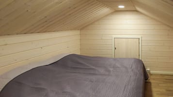 Een kamer met een schuine hemel, houten wanden, een bed met een grijze deken en een deur.