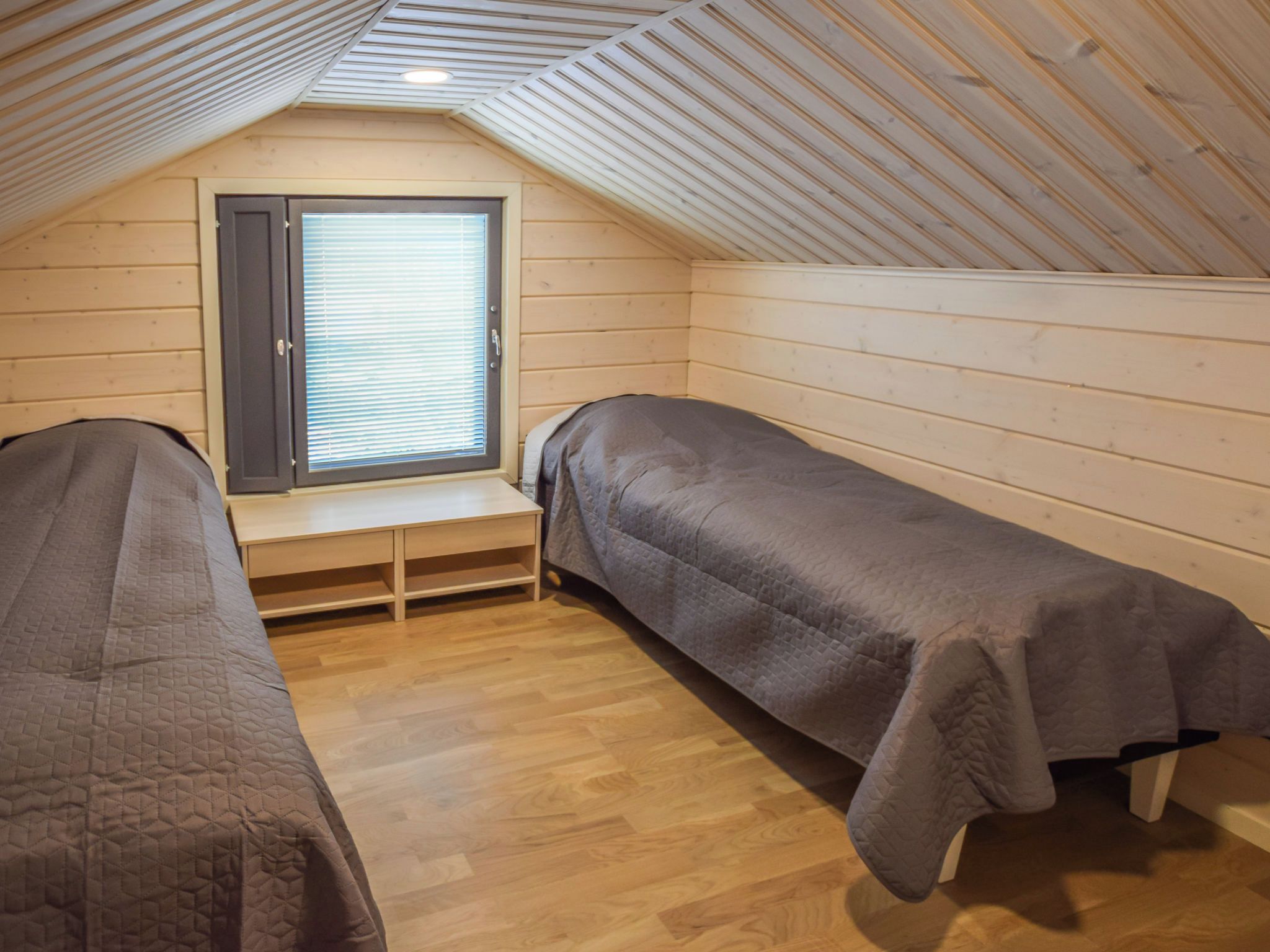 A small, single-room cabin with two beds, a window with blinds, and a sloped ceiling.