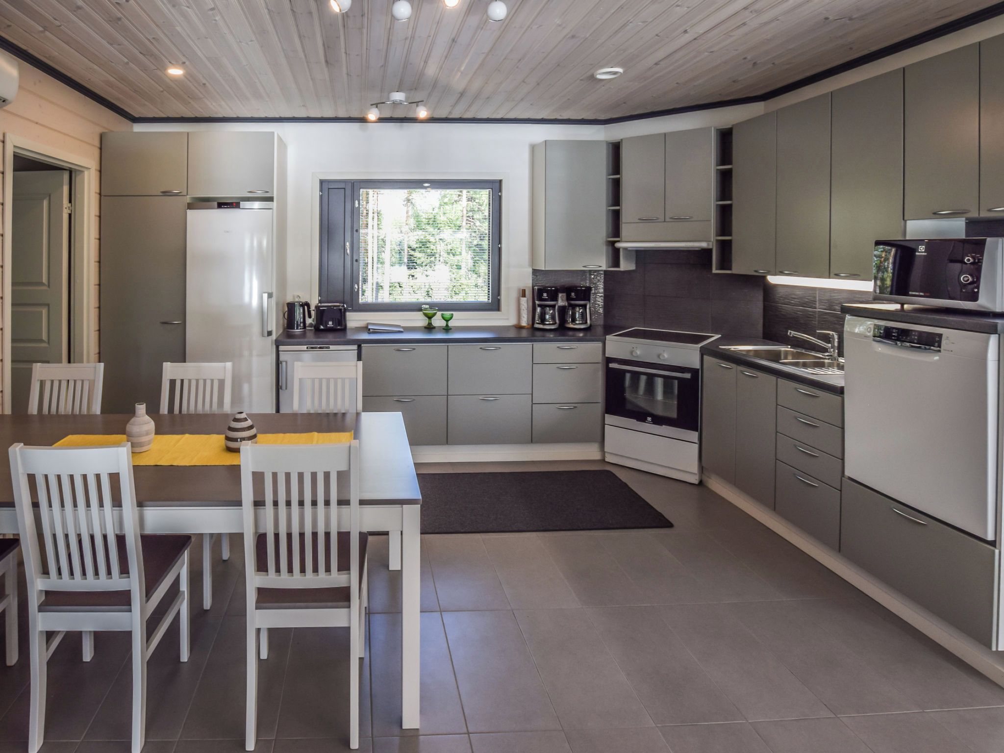 Une cuisine moderne avec des meubles gris, une table à manger avec des chaises et une fenêtre donnant sur un paysage verdoyant.
