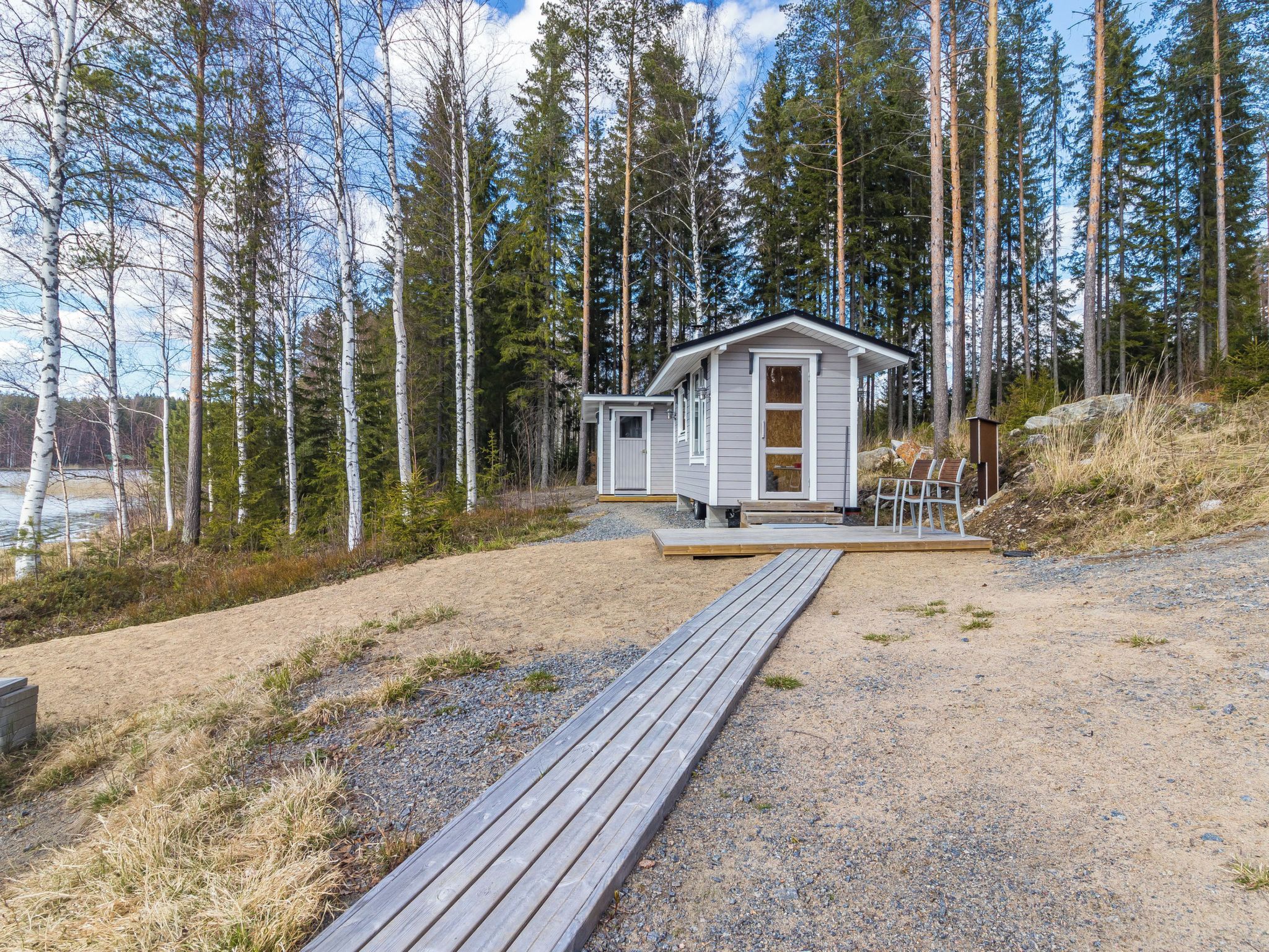 A cabin with a wooden deck leading to a door, surrounded by a forest and a body of water.