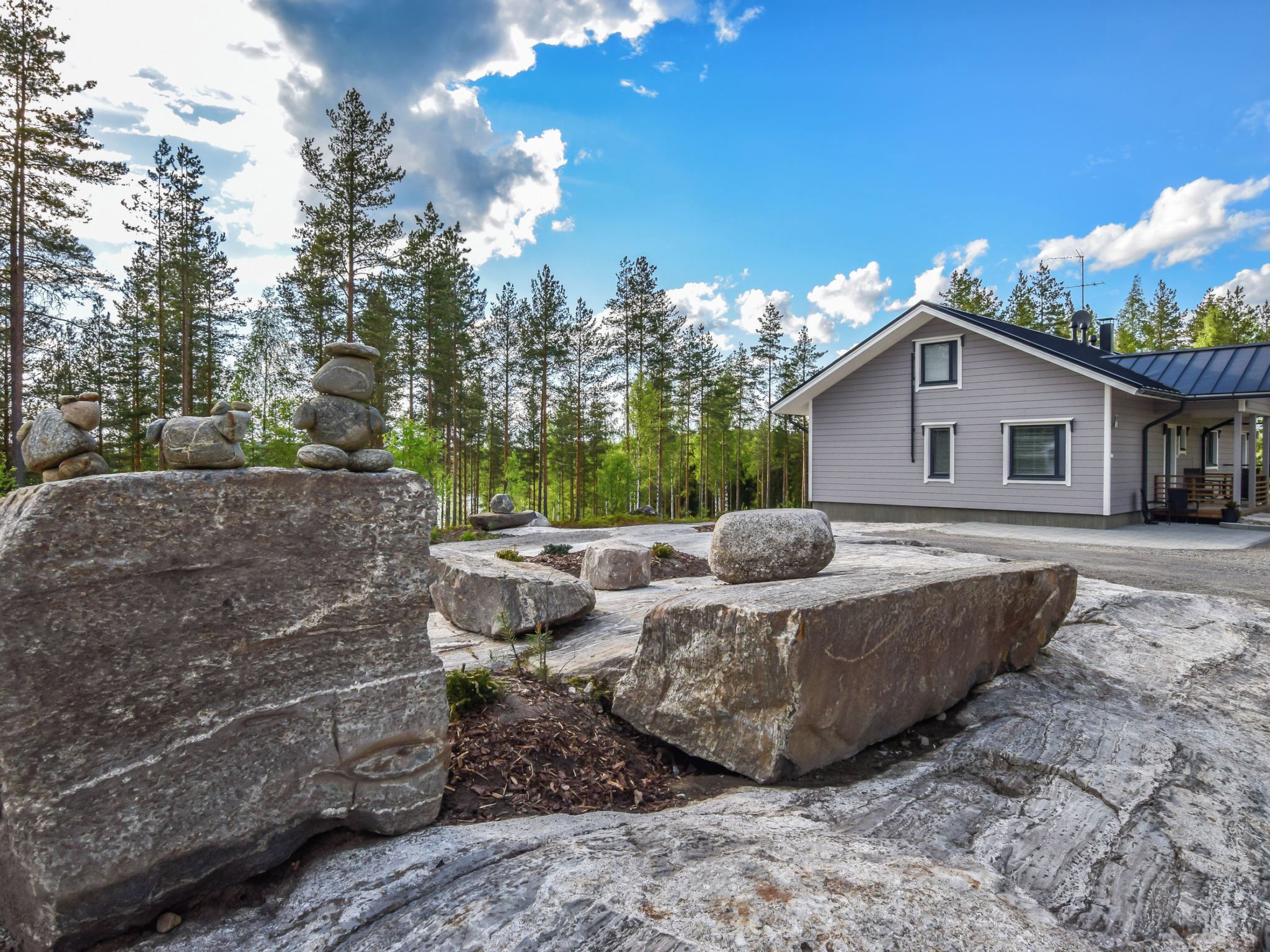 A house with a stone foundation, surrounded by a natural landscape with large rocks and pine trees.
