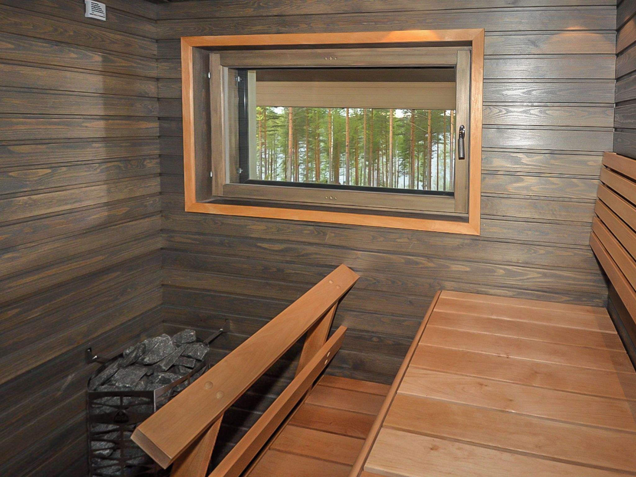 Una sauna con un banco de madera, suelo de piedra y ventana con vistas a árboles.