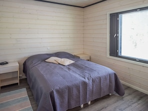 Una habitación pequeña con cama individual, ventana, mesita de noche y otra mesita auxiliar.