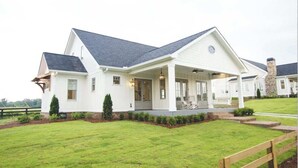 A single-story house with a covered porch, a stone chimney, and a well-maintained lawn. - Beautiful Vineyard Cottage Mtn Views (Dahlonega)