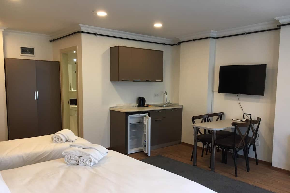 A hotel room with two beds, a kitchenette, a dining area, and a TV.