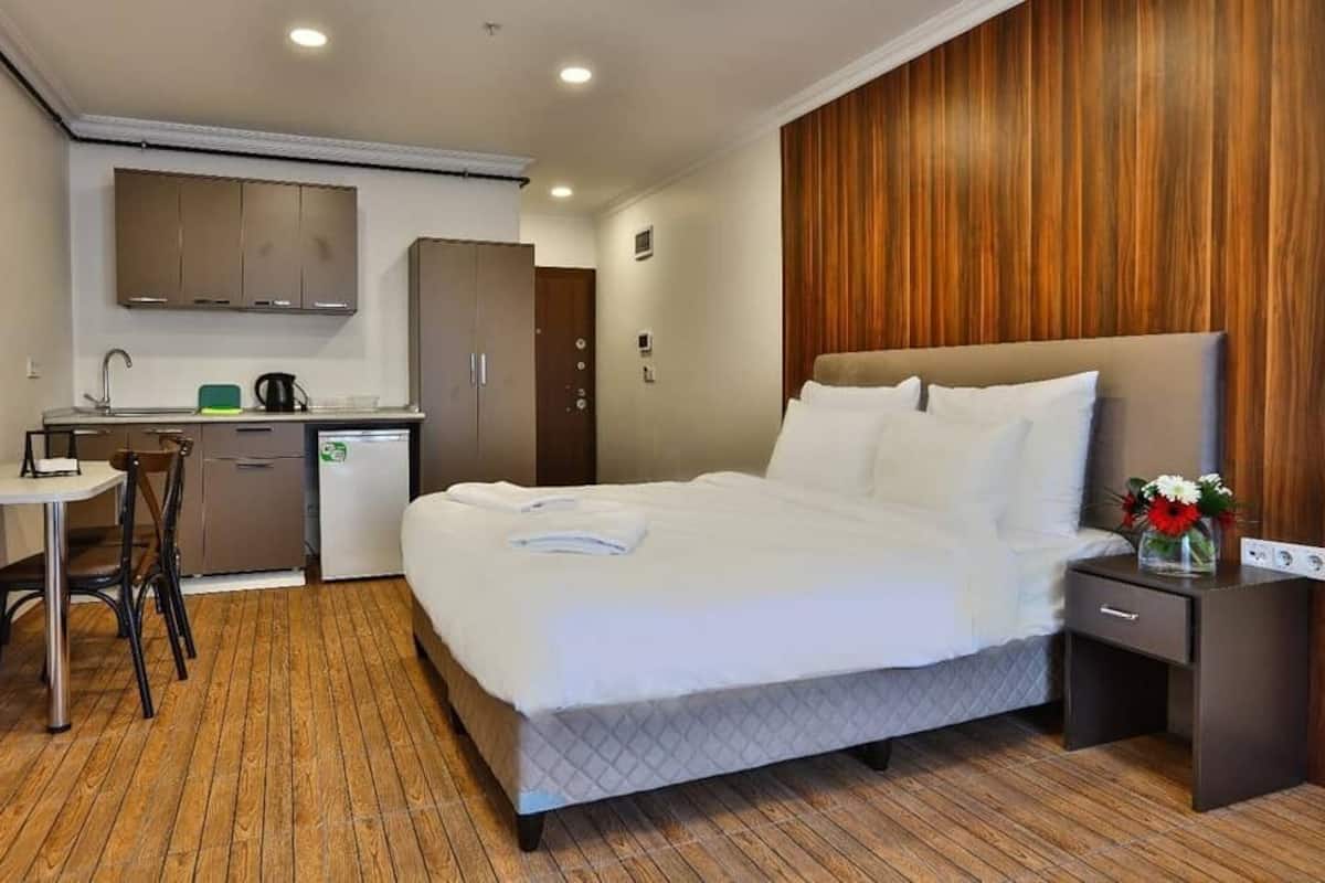A hotel room with a bed, bedside table, and a small desk area with a chair.