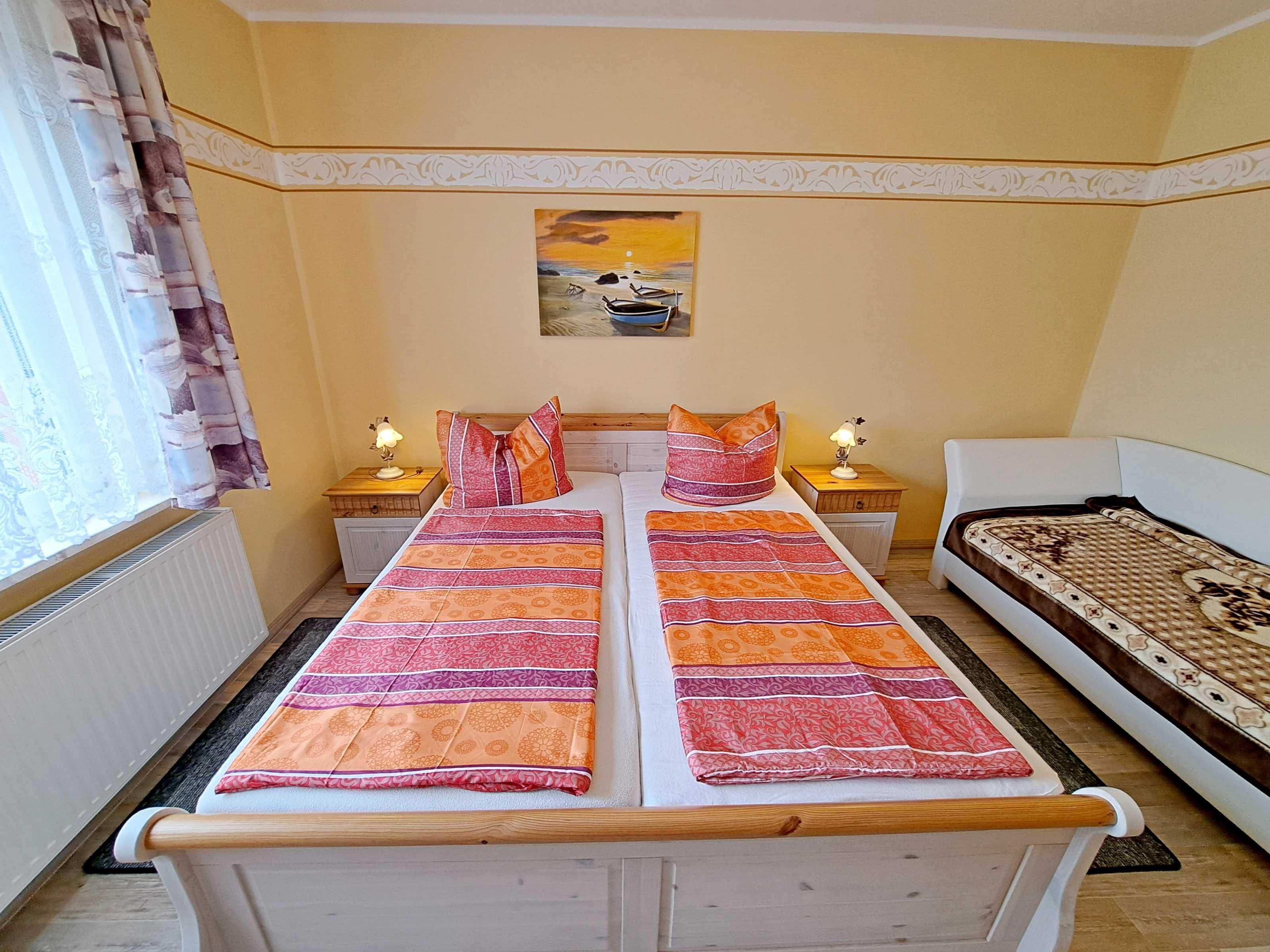 Un lit double avec une literie à motifs, deux tables de chevet avec des lampes, un tableau au mur et une fenêtre avec des rideaux.
