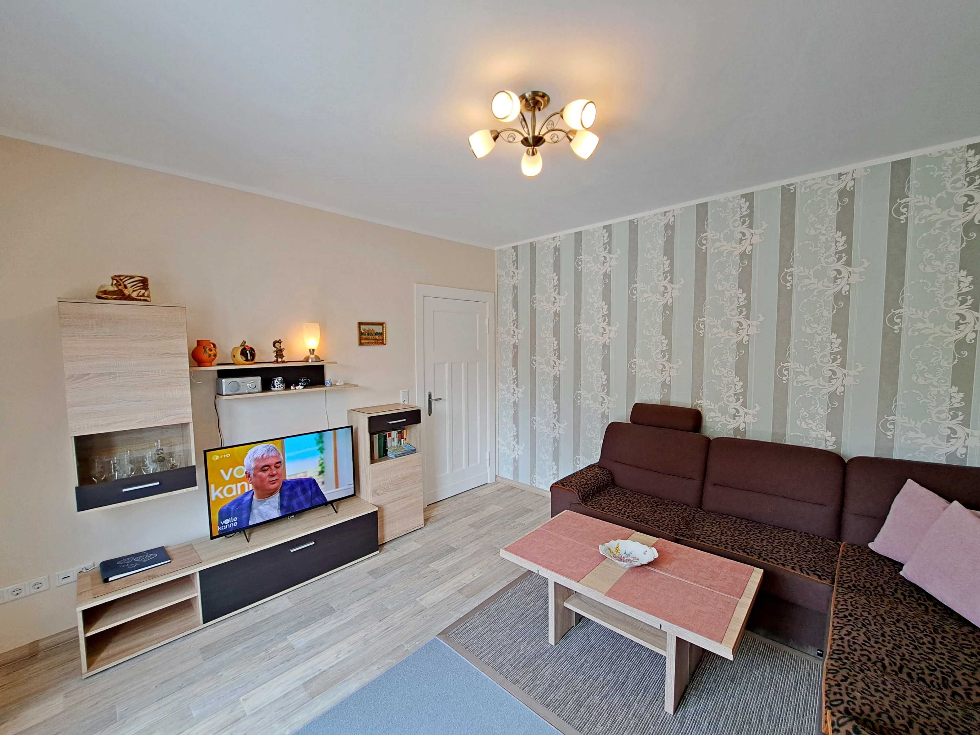 A modern living room with a flat-screen TV, a sofa, a coffee table, and a decorative ceiling light.