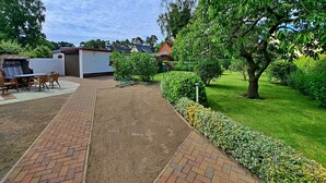 Ein Garten mit gepflastertem Weg, einem Tisch mit Stühlen und einem kleinen Gebäude mit rotem Dach.