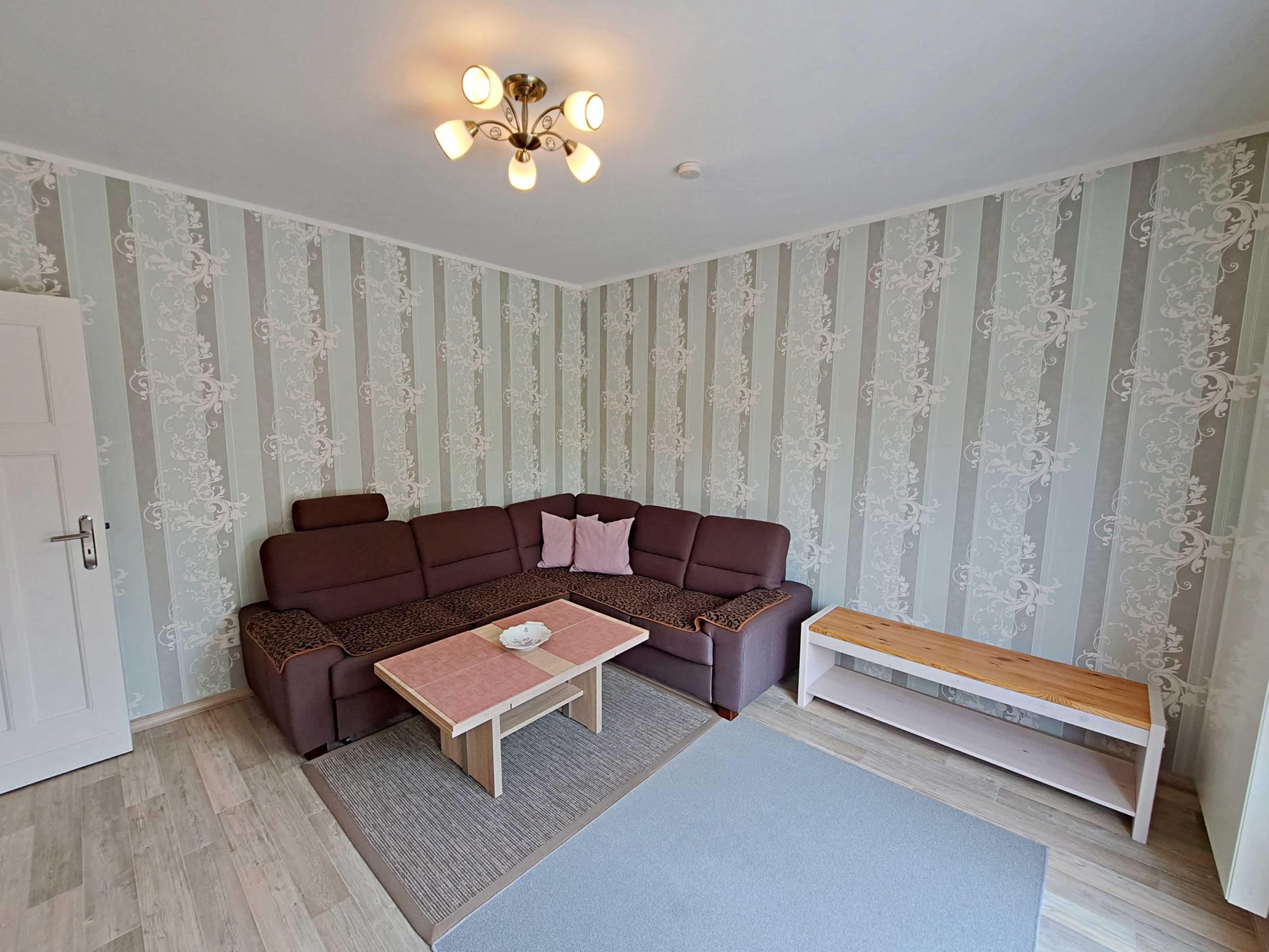 En stue med en hjørnesofa, et sofabord, en bænk og en loftlampe.