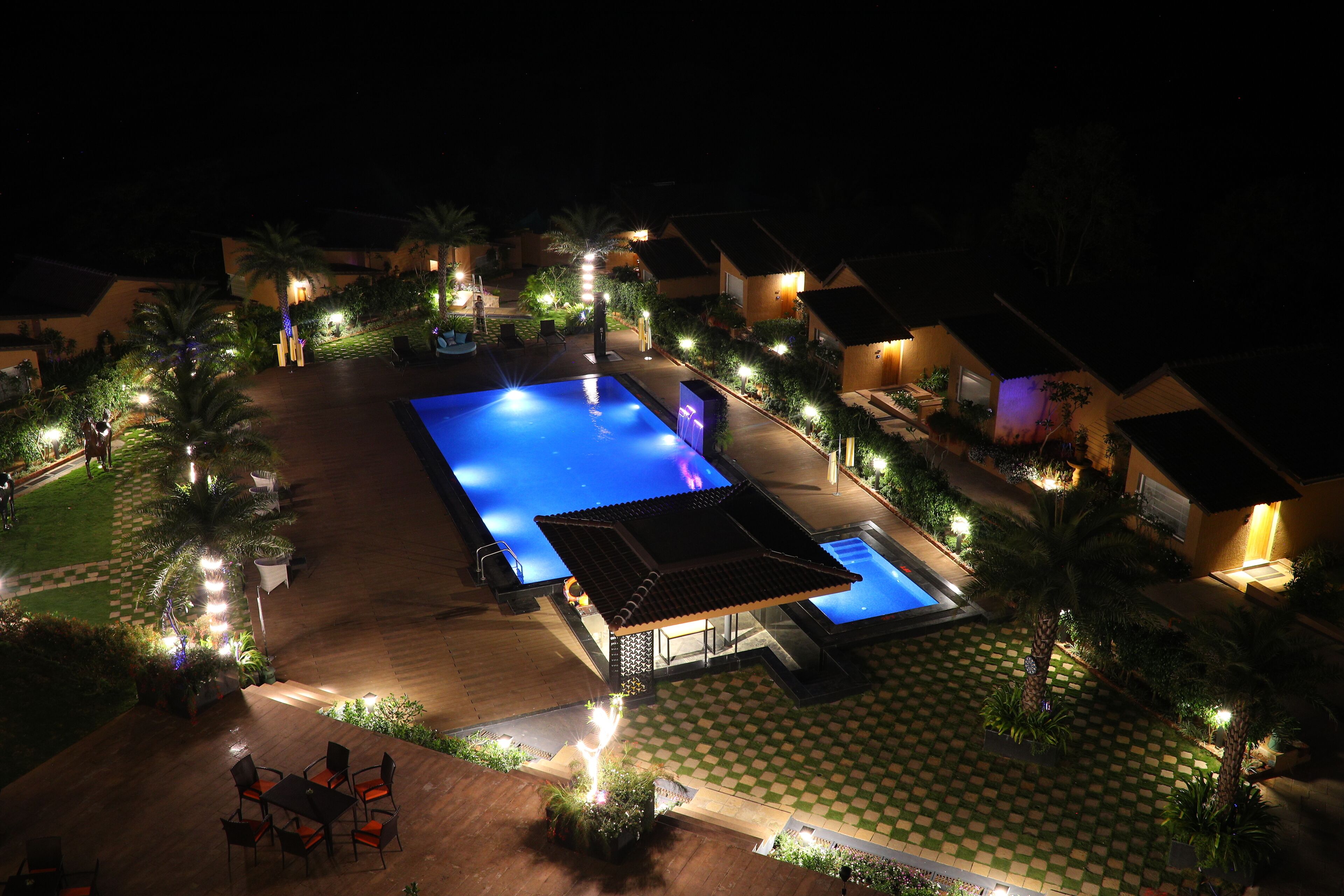 Une vue nocturne d’un complexe hôtelier doté d’une piscine, d’un espace extérieur aménagé et de chemins bien éclairés.