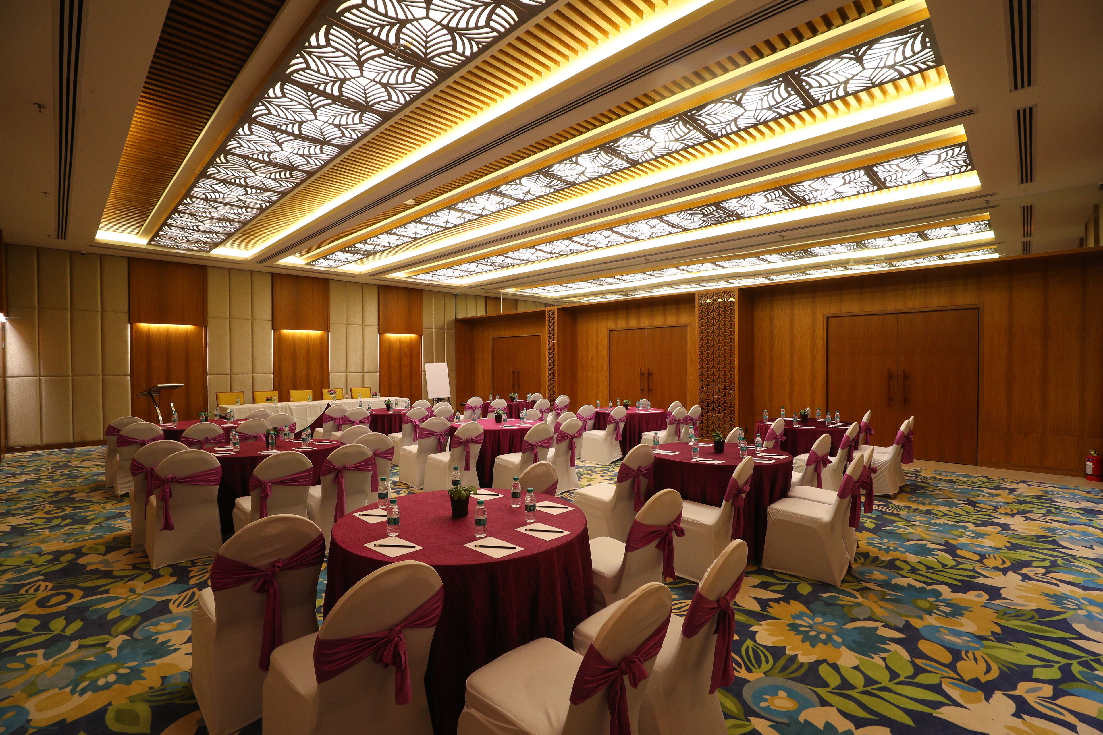 A conference room with round tables, white chairs, and a patterned carpet.