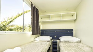Une chambre d’hôtel avec deux lits simples, une petite table et une fenêtre avec des rideaux.