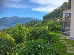 Stunning garden leads to a modern building with a balcony overlooking lush surroundings and breathtaking views.