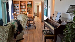 Uma sala de estar aconchegante com um piano, uma estante de livros e um espaço de refeições.