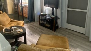 A living room with a sofa, a coffee table, a TV on a stand, and a sliding glass door leading to an outdoor area. - A Gem in the Hills - Your Secret Place From Home<br> (St. Thomas)