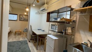Una cucina compatta con frigorifero, forno a microonde e lavello. C'è un'area pranzo con tavolo e sedie, e un piccolo tappeto sul pavimento.