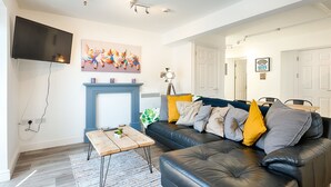 A living room with a black leather sofa, a wooden coffee table, a fireplace, and a flat-screen TV mounted on the wall. - The Nook Close to Swansea Marina (Swansea)