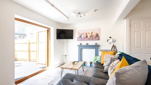 A living room with a grey sofa, a wooden coffee table, a flat-screen TV, a fireplace, and a door leading outside. - The Nook Close to Swansea Marina (Swansea)