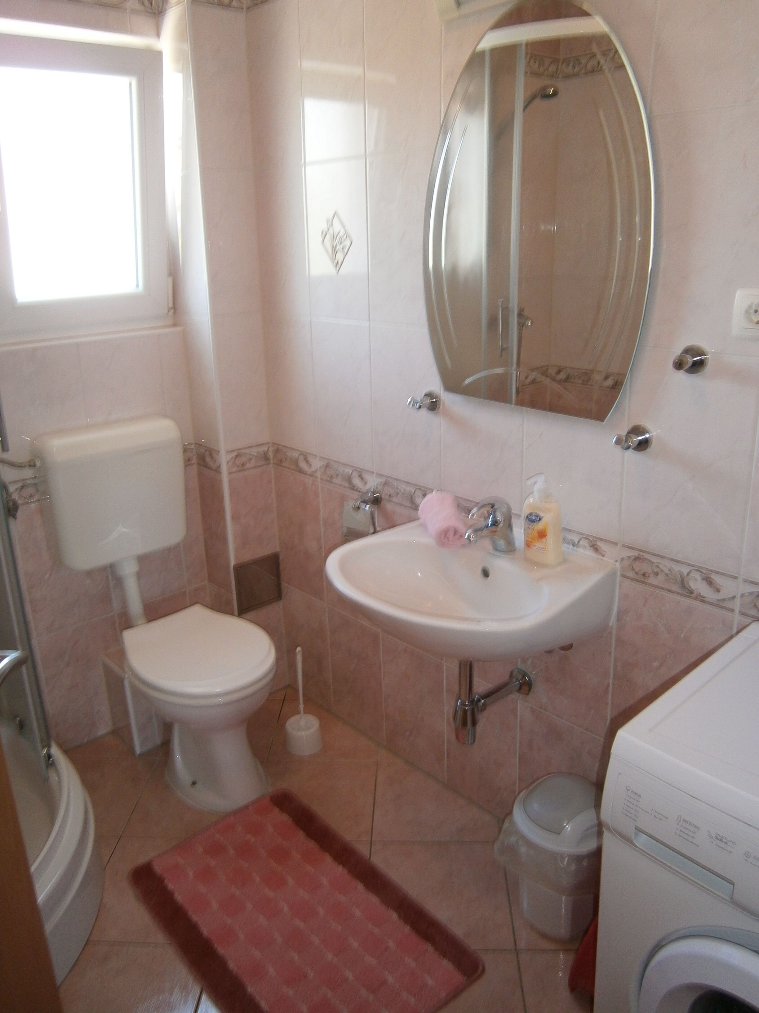 A bathroom with a toilet, sink, mirror, and a washing machine.