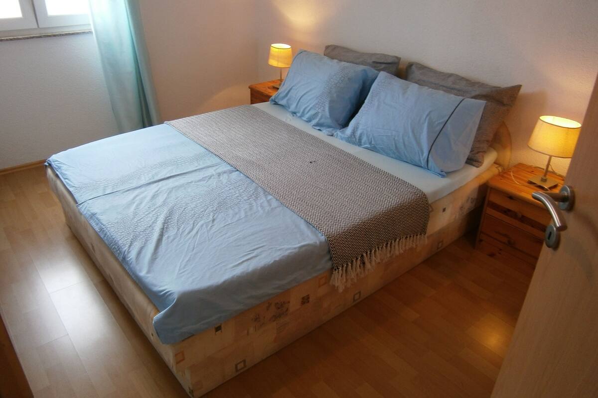 A bed with a blue bedspread and pillows, two bedside lamps, and a wooden nightstand with a drawer.