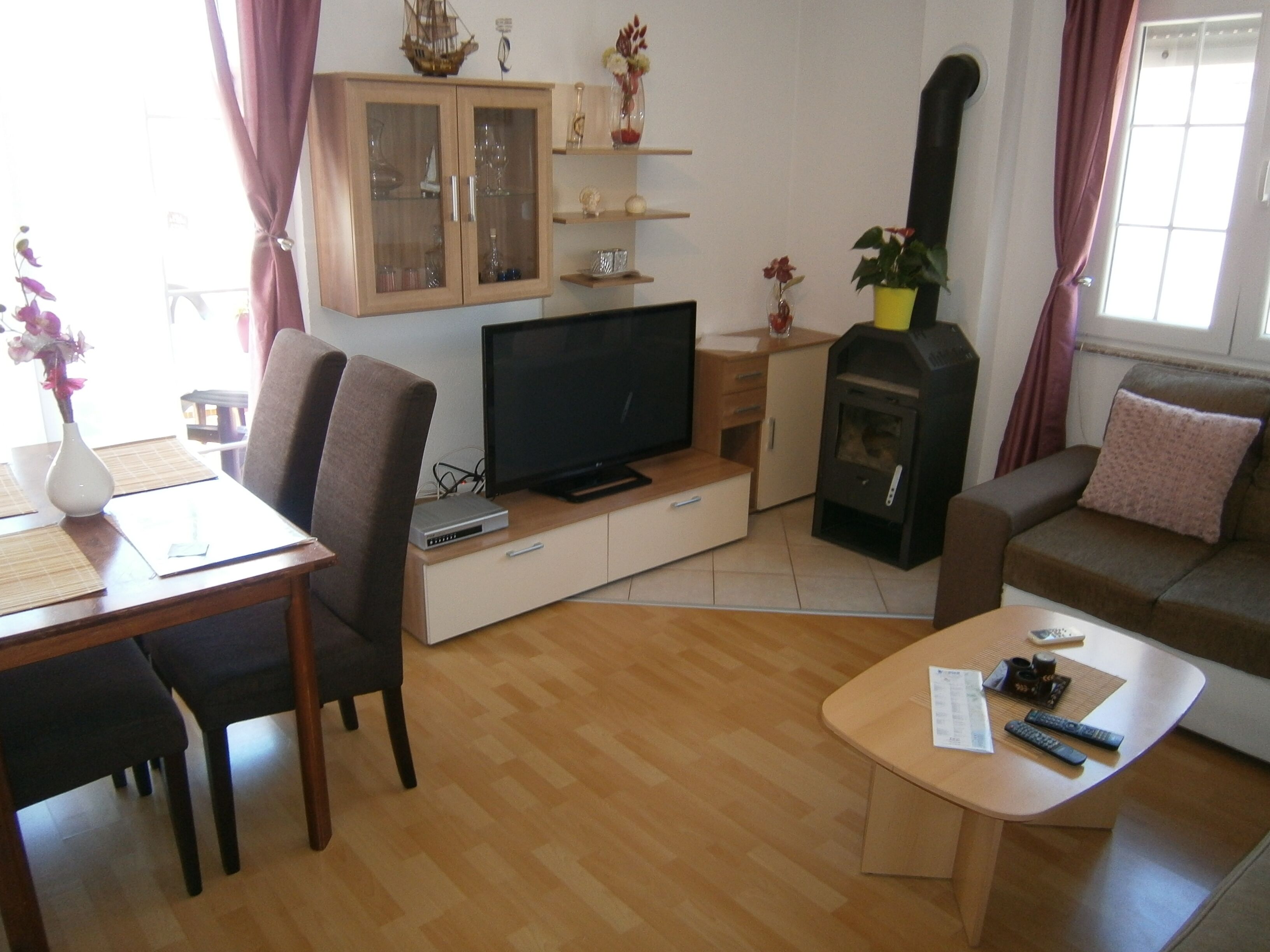 Una sala de estar con televisor, sofá, mesa de comedor con sillas, aparador con puertas de vidrio y chimenea.
