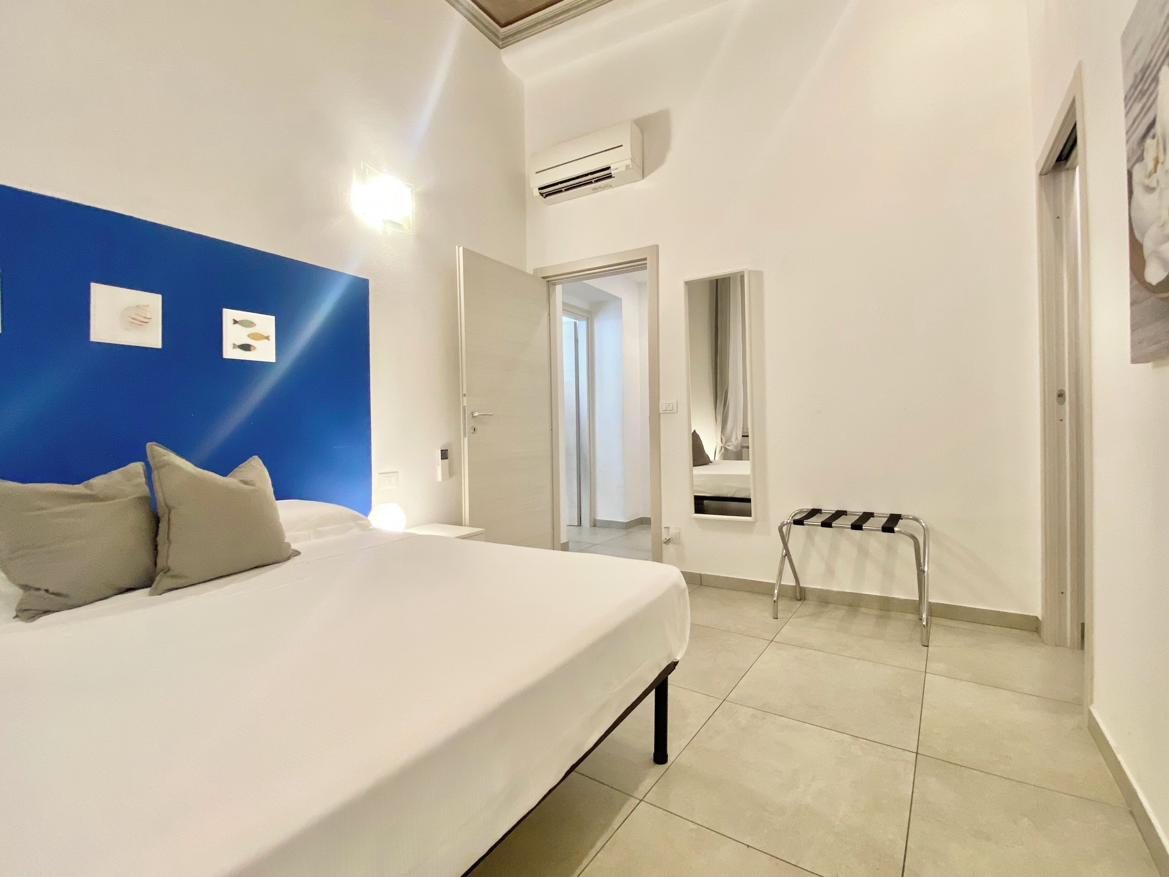 A hotel room with a large bed, a blue accent wall, a small table, and a mirror.