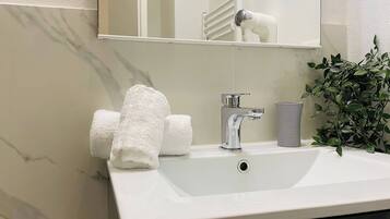 Baño con lavamanos blanco, espejo y planta en maceta.