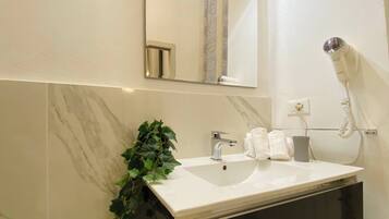 Une salle de bain avec un lavabo blanc, un miroir, un sèche-cheveux et une plante en pot.