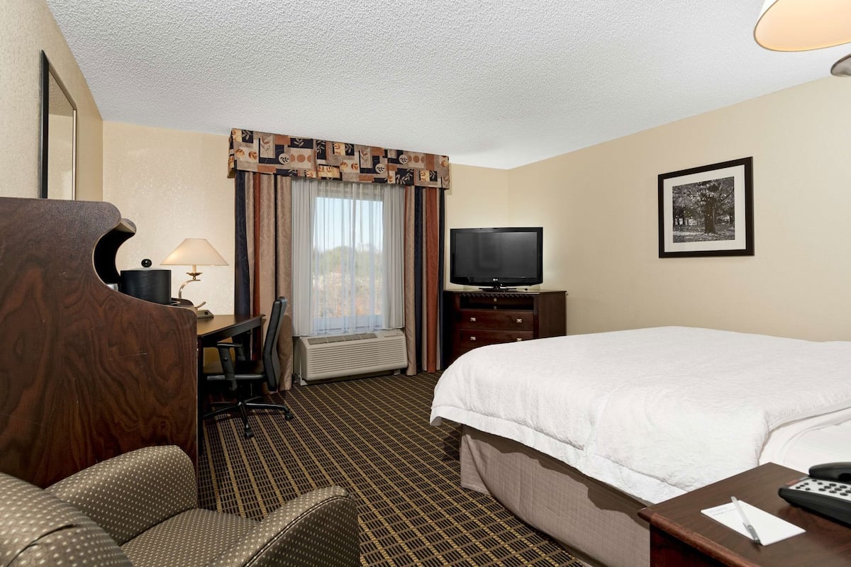 A hotel room with a bed, a desk with a chair, a television, and a framed picture on the wall.