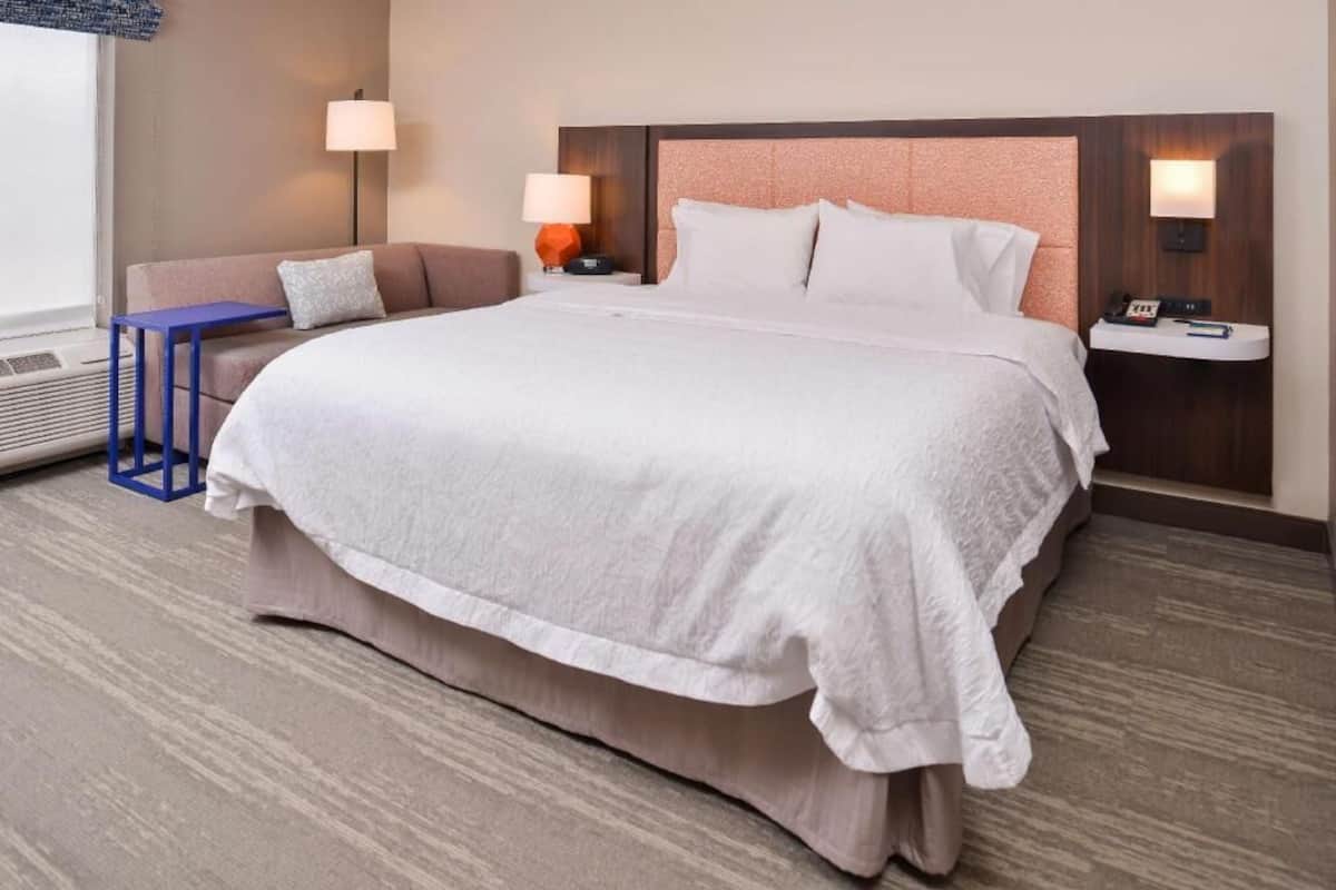 A hotel room with a large bed, two bedside tables with lamps, a small sofa, and a blue side table.