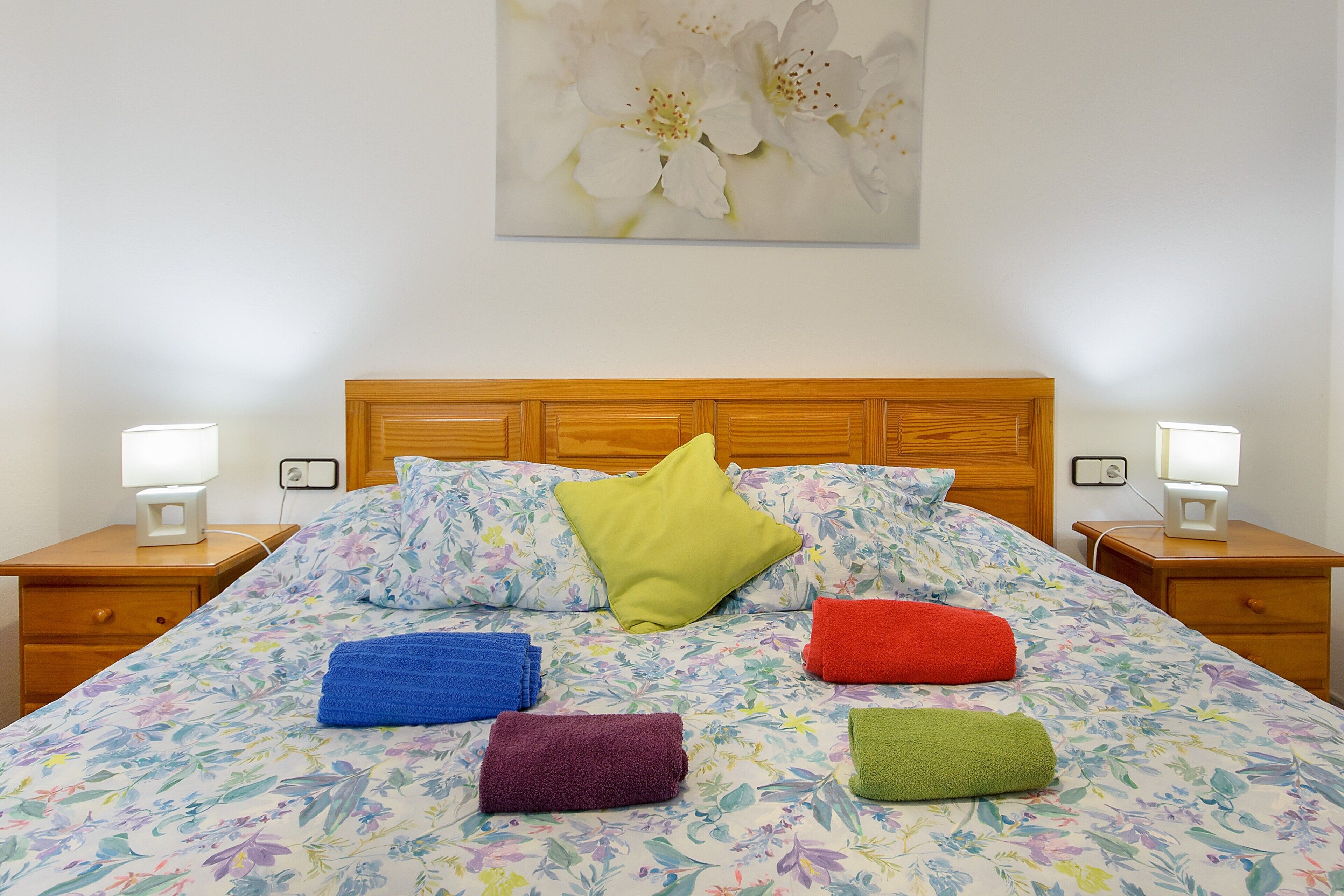 Cama com roupa de cama florida, cabeceira de madeira e várias almofadas.