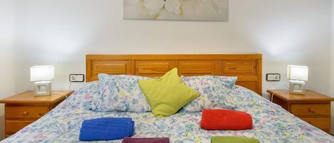 Cama com roupa de cama florida, cabeceira de madeira e várias almofadas.