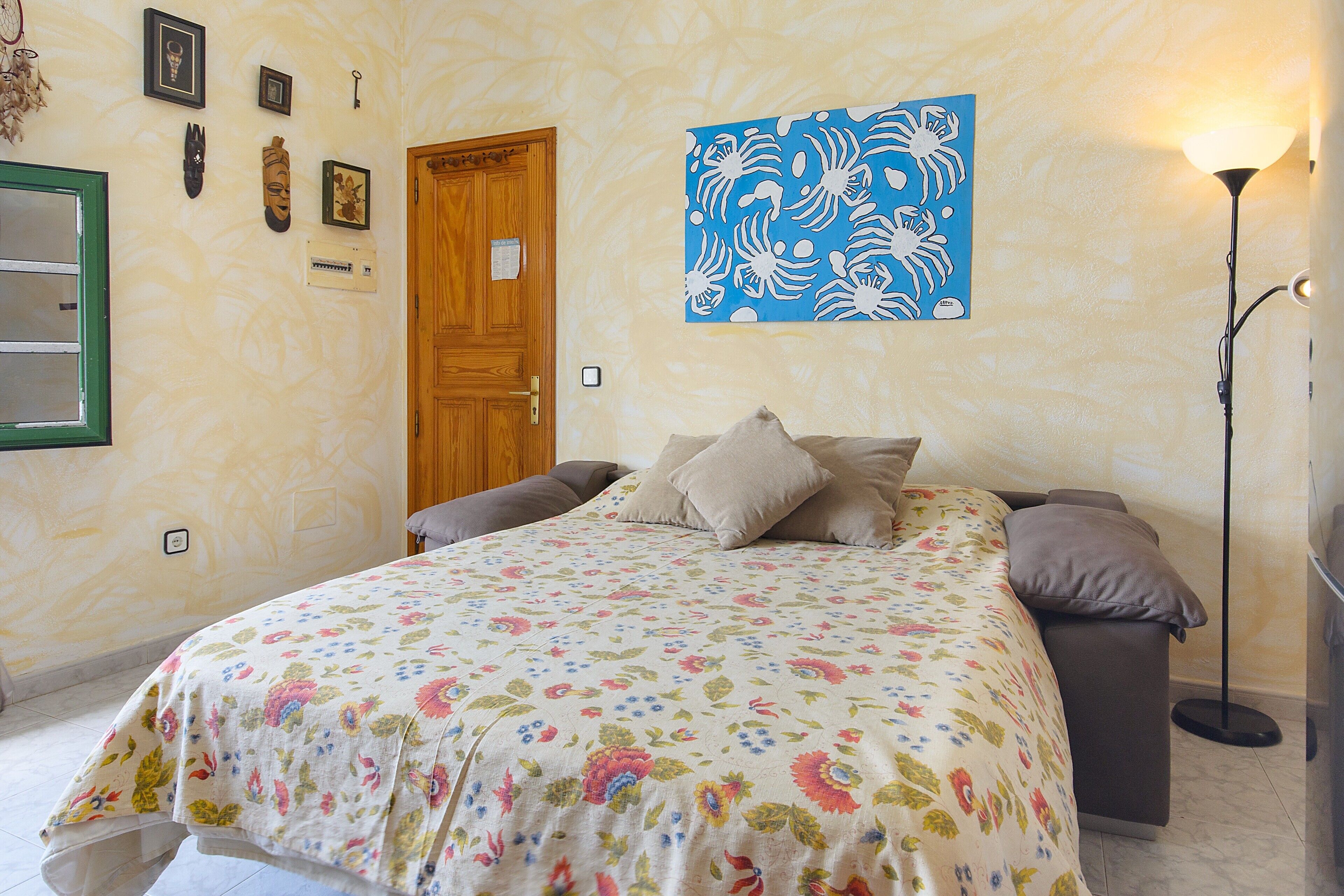 Une chambre à coucher avec un lit, une porte en bois, une œuvre d’art accrochée au mur et une lampe sur pied.