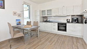 A modern kitchen with white cabinets, a built-in oven, and a dining area with a table and chairs. - Gloweglück, Germany (Glowe auf Rügen)