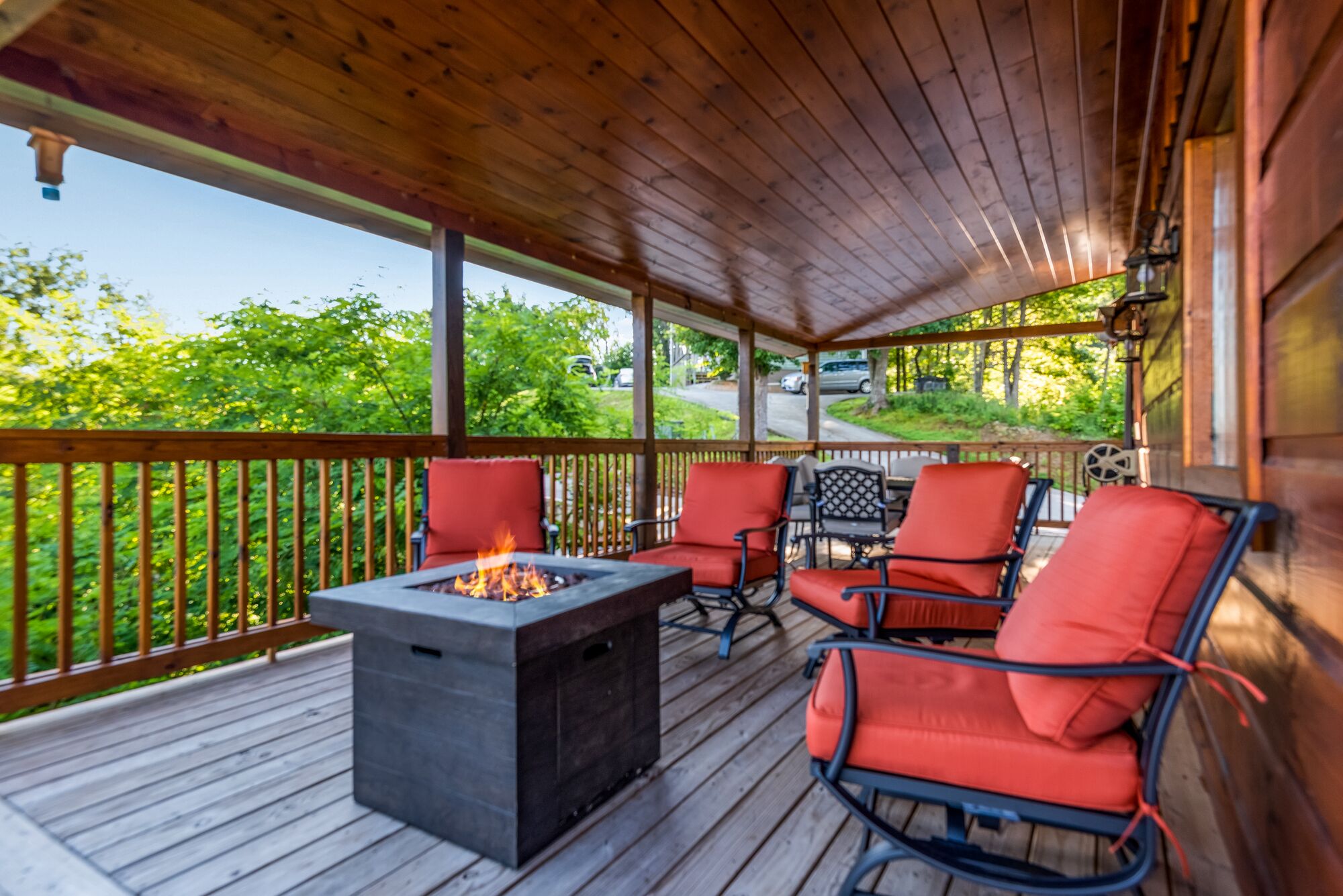 A covered outdoor deck with a fire pit, seating area, and a view of the surrounding greenery.