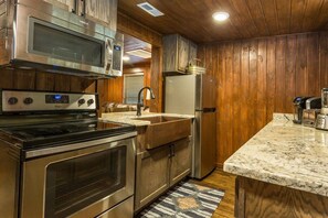 A kitchen with stainless steel appliances, wooden cabinets, a marble countertop, and a built-in oven.