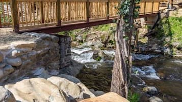 Un pont en bois enjambant un ruisseau, avec une structure en pierre en dessous, le tout entouré d’arbres et de verdure.