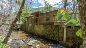 A stone-walled building with a wooden balcony overlooking a clear stream.