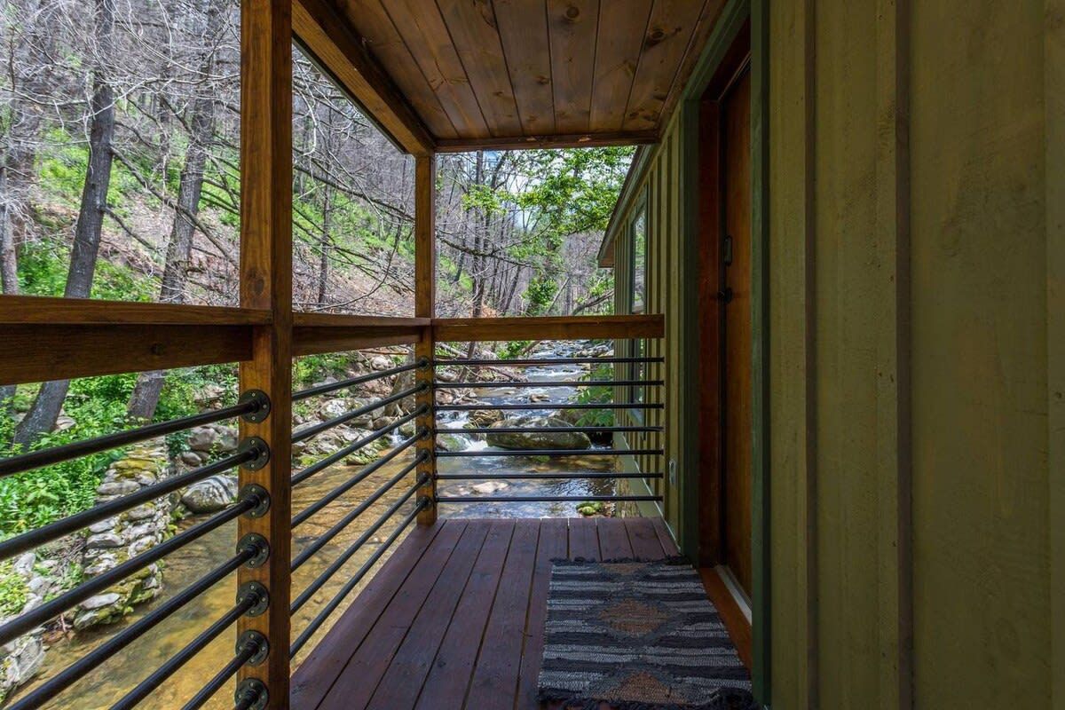 Une terrasse en bois avec une rambarde en métal, donnant sur un ruisseau et une forêt.