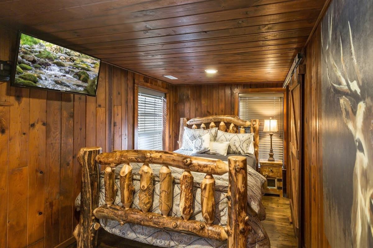 A wooden cabin bedroom with a bed, a television, and a nightstand.
