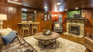 A cozy living room with a stone fireplace, wooden walls, a leather sofa, and a round coffee table.