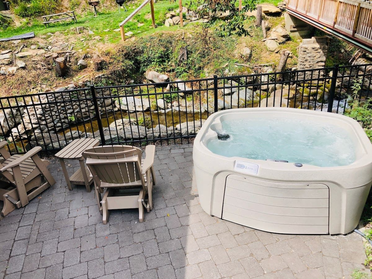 Un jacuzzi con cerco de madera, mobiliario exterior y un paisaje natural al fondo.