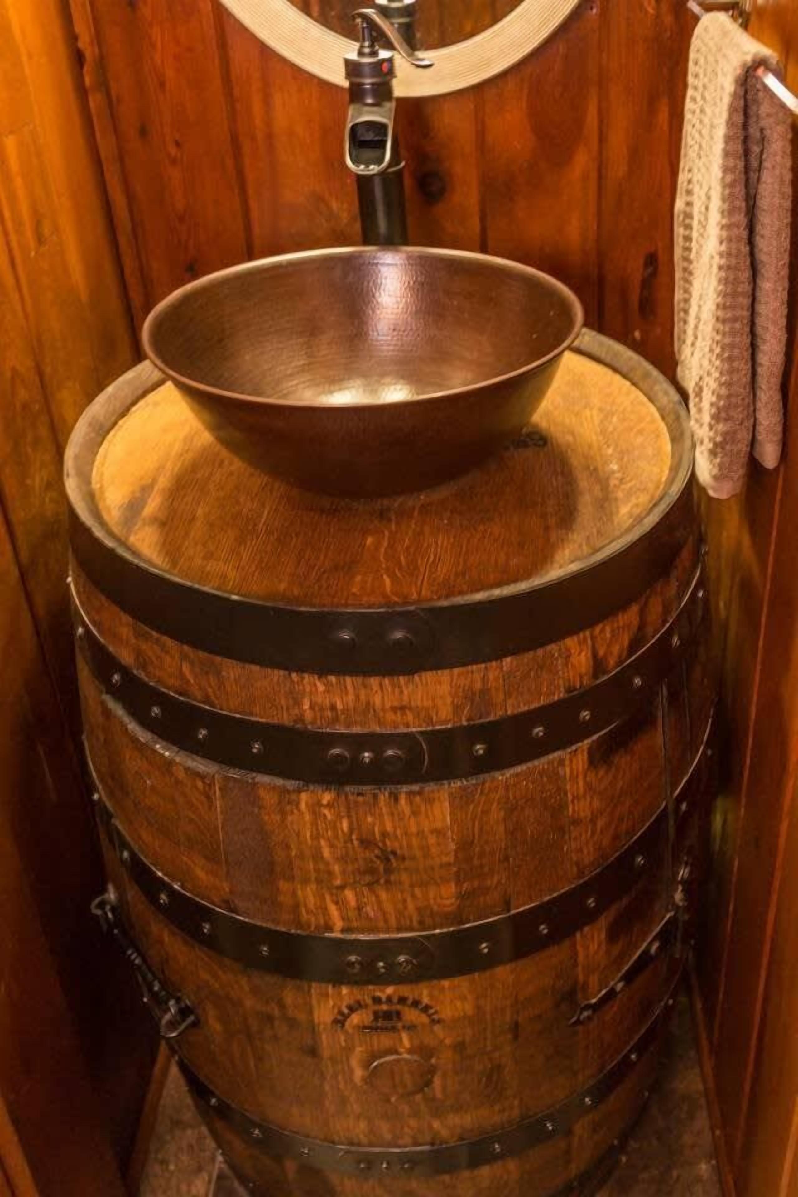 A wooden barrel with a metal bowl on top, likely a sink, in a rustic setting.