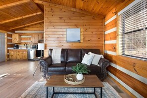Interior acogedor de una cabaña con techo de madera, un sofá de cuero, una mesa de comedor y una zona de cocina.