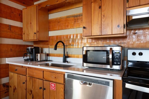 Una cocina con armarios de madera, lavavajillas de acero inoxidable, microondas, cafetera y estufa.