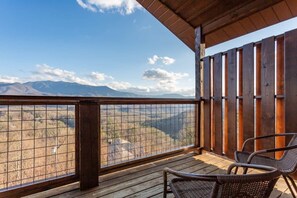 Una terraza de madera con vistas a montañas, una valla de madera y dos sillas de mimbre.